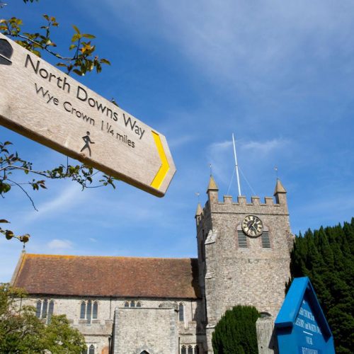 North Downs Way signpost to Wye Crown, with the village church behind